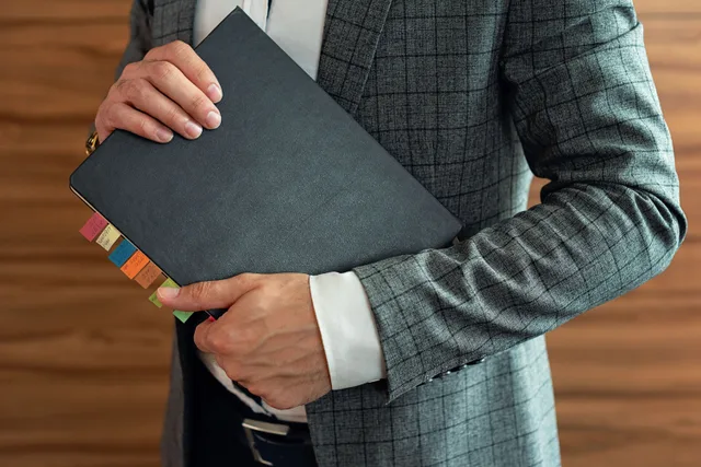 Businessperson in suit holding organized planner with tabs. Codes of conduct checklist: every item, with the reason behind it