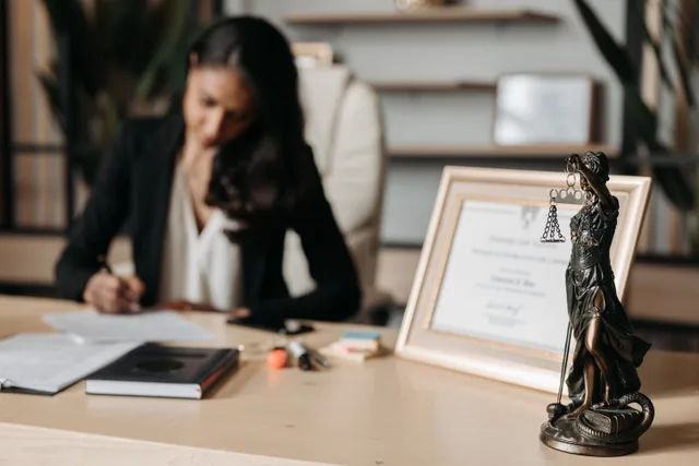 Focused woman writing at desk with Lady Justice figurine and certificate in office. Compliance Officer Personal Liability: What the DOJ Actually Looks For